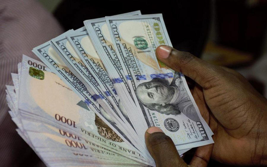 A stack of Nigerian naira banknotes next to a US dollar bill
